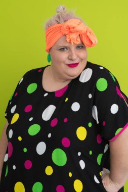 Artı canlı polka noktalı kıyafetli cüsseli kadın uzanmış elleri ve komik ifadesiyle komik omuz silkme hareketi yapıyor. 