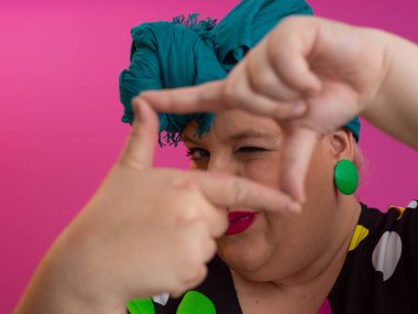 Yaratıcı artı cüsseli kadın parmaklarıyla dikdörtgen yapıyor, pembe arka planda kamera görüntüleyicisi canlandırıyor.. 