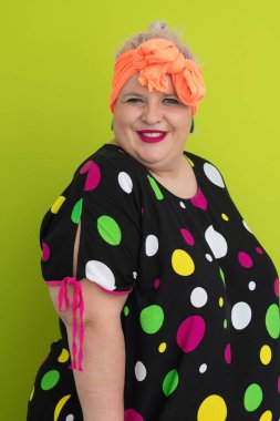 Artı canlı polka noktalı kıyafetli cüsseli kadın uzanmış elleri ve komik ifadesiyle komik omuz silkme hareketi yapıyor. 