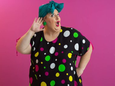 Expressive plus size woman in colorful polka dot dress raising hands in humorous surprise against vibrant pink background.  clipart
