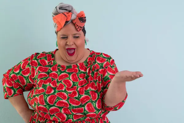 Karpuz desenli elbisesiyle açık avucuna komik ve şaşkın bakışlı açık mavi arkaplana bakan etkileyici ve iri yarı kadın.. 