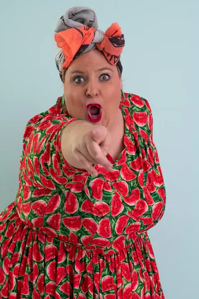 Ayrıca renkli karpuz temalı elbisesi ve turuncu başlıklı, etkilenmemiş yüz ifadesi ve pastel mavisi arka planda kalçaları olan bir kadın.. 