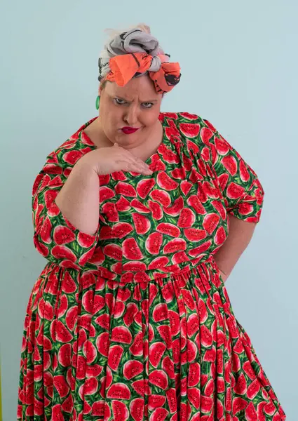 Ayrıca renkli karpuz temalı elbisesi ve turuncu başlıklı, etkilenmemiş yüz ifadesi ve pastel mavisi arka planda kalçaları olan bir kadın.. 