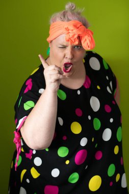 Artı canlı polka noktalı kıyafetli cüsseli kadın uzanmış elleri ve komik ifadesiyle komik omuz silkme hareketi yapıyor. 