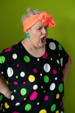 Artı canlı polka noktalı kıyafetli cüsseli kadın uzanmış elleri ve komik ifadesiyle komik omuz silkme hareketi yapıyor. 