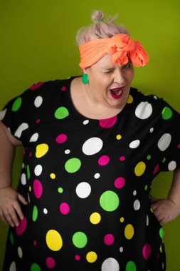 Artı canlı polka noktalı kıyafetli cüsseli kadın uzanmış elleri ve komik ifadesiyle komik omuz silkme hareketi yapıyor. 