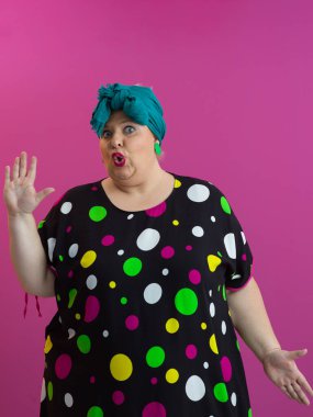 Expressive plus size woman in colorful polka dot dress raising hands in humorous surprise against vibrant pink background.  clipart