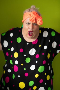 Artı canlı polka noktalı kıyafetli cüsseli kadın uzanmış elleri ve komik ifadesiyle komik omuz silkme hareketi yapıyor. 