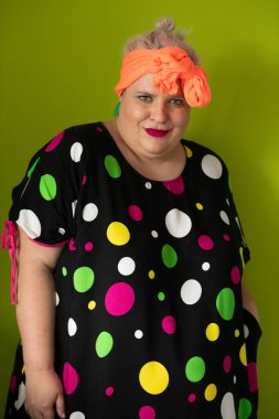 Artı canlı polka noktalı kıyafetli cüsseli kadın uzanmış elleri ve komik ifadesiyle komik omuz silkme hareketi yapıyor. 