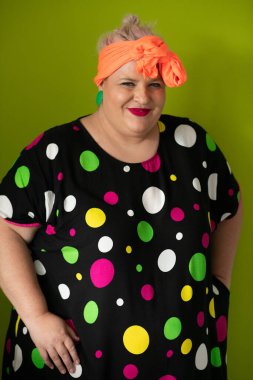 Artı canlı polka noktalı kıyafetli cüsseli kadın uzanmış elleri ve komik ifadesiyle komik omuz silkme hareketi yapıyor. 