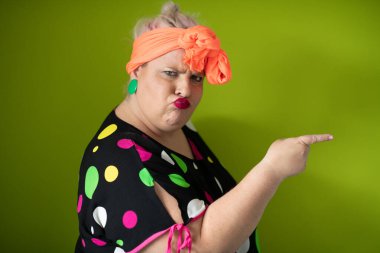 Artı canlı polka noktalı kıyafetli cüsseli kadın uzanmış elleri ve komik ifadesiyle komik omuz silkme hareketi yapıyor. 