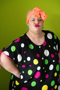 Artı canlı polka noktalı kıyafetli cüsseli kadın uzanmış elleri ve komik ifadesiyle komik omuz silkme hareketi yapıyor. 