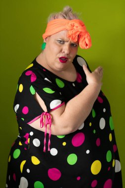 Artı canlı polka noktalı kıyafetli cüsseli kadın uzanmış elleri ve komik ifadesiyle komik omuz silkme hareketi yapıyor. 