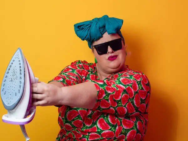 Güneş gözlüğü takan, karpuz elbisesi giyen, tabanca gibi demir tutan, neşeli turuncu arka planı olan, neşeli ve kendinden emin bir kadın..