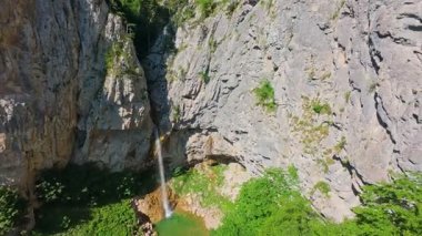 Bereketli yeşil ağaçlar ve ormanlarla çevrili kayalık bir uçurumdan şelalenin havadan görünüşü güneşli bir yaz gününde yumuşak FPV insansız hava aracıyla çekilmiştir, doğa için mükemmeldir.