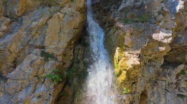 Bereketli yeşil ağaçlar ve ormanlarla çevrili kayalık bir uçurumdan şelalenin havadan görünüşü güneşli bir yaz gününde yumuşak FPV insansız hava aracıyla çekilmiştir, doğa için mükemmeldir.