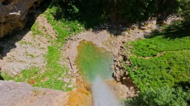 Bereketli yeşil ağaçlar ve ormanlarla çevrili kayalık bir uçurumdan şelalenin havadan görünüşü güneşli bir yaz gününde yumuşak FPV insansız hava aracıyla çekilmiştir, doğa için mükemmeldir.