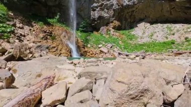 Bereketli yeşil ağaçlar ve ormanlarla çevrili kayalık bir uçurumdan şelalenin havadan görünüşü güneşli bir yaz gününde yumuşak FPV insansız hava aracıyla çekilmiştir, doğa için mükemmeldir.