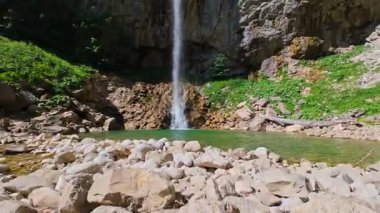 Bereketli yeşil ağaçlar ve ormanlarla çevrili kayalık bir uçurumdan şelalenin havadan görünüşü güneşli bir yaz gününde yumuşak FPV insansız hava aracıyla çekilmiştir, doğa için mükemmeldir.