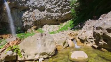Bereketli yeşil ağaçlar ve ormanlarla çevrili kayalık bir uçurumdan şelalenin havadan görünüşü güneşli bir yaz gününde yumuşak FPV insansız hava aracıyla çekilmiştir, doğa için mükemmeldir.