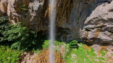 Bereketli yeşil ağaçlar ve ormanlarla çevrili kayalık bir uçurumdan şelalenin havadan görünüşü güneşli bir yaz gününde yumuşak FPV insansız hava aracıyla çekilmiştir, doğa için mükemmeldir.