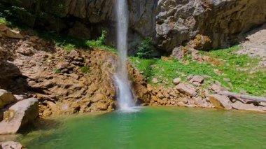 Bereketli yeşil ağaçlar ve ormanlarla çevrili kayalık bir uçurumdan şelalenin havadan görünüşü güneşli bir yaz gününde yumuşak FPV insansız hava aracıyla çekilmiştir, doğa için mükemmeldir.