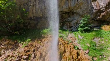 Bereketli yeşil ağaçlar ve ormanlarla çevrili kayalık bir uçurumdan şelalenin havadan görünüşü güneşli bir yaz gününde yumuşak FPV insansız hava aracıyla çekilmiştir, doğa için mükemmeldir.