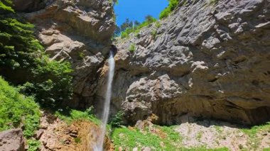 Bereketli yeşil ağaçlar ve ormanlarla çevrili kayalık bir uçurumdan şelalenin havadan görünüşü güneşli bir yaz gününde yumuşak FPV insansız hava aracıyla çekilmiştir, doğa için mükemmeldir.