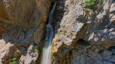 Bereketli yeşil ağaçlar ve ormanlarla çevrili kayalık bir uçurumdan şelalenin havadan görünüşü güneşli bir yaz gününde yumuşak FPV insansız hava aracıyla çekilmiştir, doğa için mükemmeldir.