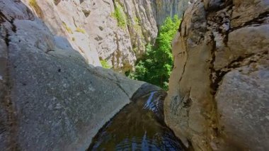 Bereketli yeşil ağaçlar ve ormanlarla çevrili kayalık bir uçurumdan şelalenin havadan görünüşü güneşli bir yaz gününde yumuşak FPV insansız hava aracıyla çekilmiştir, doğa için mükemmeldir.