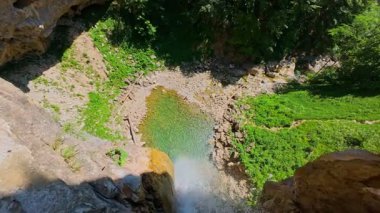 Bereketli yeşil ağaçlar ve ormanlarla çevrili kayalık bir uçurumdan şelalenin havadan görünüşü güneşli bir yaz gününde yumuşak FPV insansız hava aracıyla çekilmiştir, doğa için mükemmeldir.