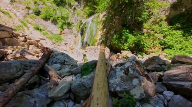 Bereketli yeşil ağaçlar ve ormanlarla çevrili kayalık bir uçurumdan şelalenin havadan görünüşü güneşli bir yaz gününde yumuşak FPV insansız hava aracıyla çekilmiştir, doğa için mükemmeldir.