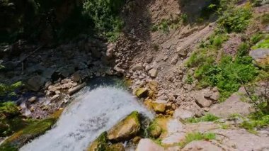 Bereketli yeşil ağaçlar ve ormanlarla çevrili kayalık bir uçurumdan şelalenin havadan görünüşü güneşli bir yaz gününde yumuşak FPV insansız hava aracıyla çekilmiştir, doğa için mükemmeldir.