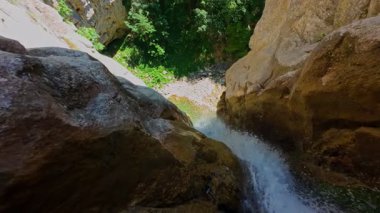 Bereketli yeşil ağaçlar ve ormanlarla çevrili kayalık bir uçurumdan şelalenin havadan görünüşü güneşli bir yaz gününde yumuşak FPV insansız hava aracıyla çekilmiştir, doğa için mükemmeldir.