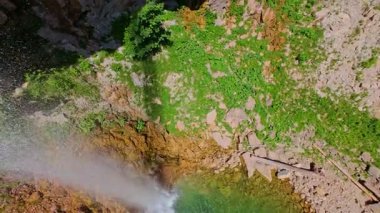 Bereketli yeşil ağaçlar ve ormanlarla çevrili kayalık bir uçurumdan şelalenin havadan görünüşü güneşli bir yaz gününde yumuşak FPV insansız hava aracıyla çekilmiştir, doğa için mükemmeldir.