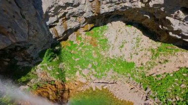 Bereketli yeşil ağaçlar ve ormanlarla çevrili kayalık bir uçurumdan şelalenin havadan görünüşü güneşli bir yaz gününde yumuşak FPV insansız hava aracıyla çekilmiştir, doğa için mükemmeldir.