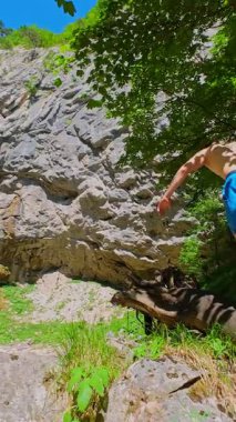 Güneşli bir günde yemyeşil orman ve kayalarla çevrili temiz bir dağ nehrinde yüzen bir kadının FPV drone görüntüsü. Vahşi doğada yaz kaçamağı, macera ve seyahat için ideal.. 