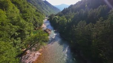 Berrak yeşil bir nehrin havadan görünüşü yemyeşil bir orman ve dağ vadisinde akıyor. İnsanlar canlı bir mavi gökyüzü kaçışı altında bir çakıl taşı plajında dinleniyor.