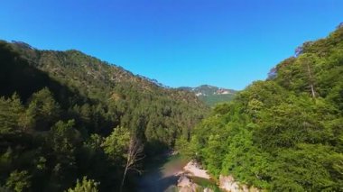 Berrak yeşil bir nehrin havadan görünüşü yemyeşil bir orman ve dağ vadisinde akıyor. İnsanlar canlı bir mavi gökyüzü kaçışı altında bir çakıl taşı plajında dinleniyor.