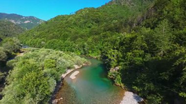 Berrak yeşil bir nehrin havadan görünüşü yemyeşil bir orman ve dağ vadisinde akıyor. İnsanlar canlı bir mavi gökyüzü kaçışı altında bir çakıl taşı plajında dinleniyor.