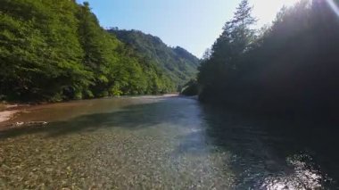 Berrak yeşil bir nehrin havadan görünüşü yemyeşil bir orman ve dağ vadisinde akıyor. İnsanlar canlı bir mavi gökyüzü kaçışı altında bir çakıl taşı plajında dinleniyor.