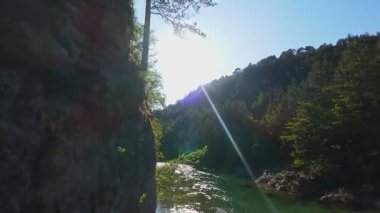 Berrak yeşil bir nehrin havadan görünüşü yemyeşil bir orman ve dağ vadisinde akıyor. İnsanlar canlı bir mavi gökyüzü kaçışı altında bir çakıl taşı plajında dinleniyor.