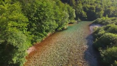 Berrak yeşil bir nehrin havadan görünüşü yemyeşil bir orman ve dağ vadisinde akıyor. İnsanlar canlı bir mavi gökyüzü kaçışı altında bir çakıl taşı plajında dinleniyor.