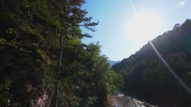 Berrak yeşil bir nehrin havadan görünüşü yemyeşil bir orman ve dağ vadisinde akıyor. İnsanlar canlı bir mavi gökyüzü kaçışı altında bir çakıl taşı plajında dinleniyor.