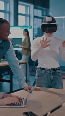 Modern bir iş yerinde çalışan tekerlekli sandalyedeki engelli bir iş kadını. Çevredeki ekip sanal gerçeklik gözlükleri kullanıyor, açık alan yaratıcılığında en son teknolojiyle işbirliği yapıyorlar.