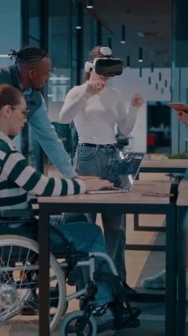 Modern bir iş yerinde çalışan tekerlekli sandalyedeki engelli bir iş kadını. Çevredeki ekip sanal gerçeklik gözlükleri kullanıyor, açık alan yaratıcılığında en son teknolojiyle işbirliği yapıyorlar.