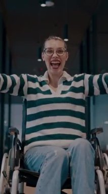 Tekerlekli sandalyede engelli neşeli bir kadın modern bir ofis, kapsamlı bir iş yeri, güç, başarı, erişilebilirlik ve dinamik bir pozitiflikte kollarını kaldırıyor.