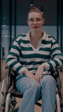 Tekerlekli sandalyede engelli neşeli bir kadın modern bir ofis, kapsamlı bir iş yeri, güç, başarı, erişilebilirlik ve dinamik bir pozitiflikte kollarını kaldırıyor.