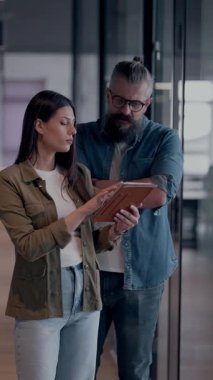 Üst düzey bir hipster akıl hocası ve Avrupalı bir lider, modern bir çalışma alanında tablet üzerinde çalışırken, arka planda yoğun meslektaşlar çalışırken güvenli bir şekilde işbirliği yaparak bir projeyi tartışıyorlar.