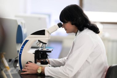 Parlak, modern bir laboratuvarda mikroskopla numuneleri inceleyen doktor bilim adamına yakın durun..